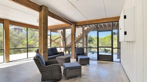 Ein geräumiges Zimmer mit großen Fenstern, Korbmöbeln und einem Betonboden.