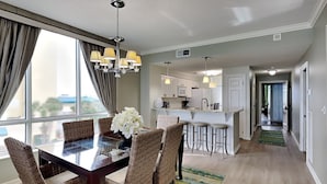 A modern kitchen with white cabinets, a central island with bar stools, and a dining area with wicker chairs and a glass table.