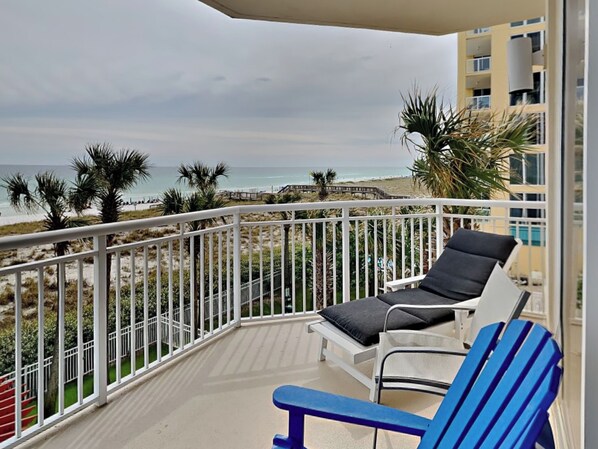 Un balcon avec une balustrade blanche, une chaise bleue et une chaise longue blanche avec un coussin noir.