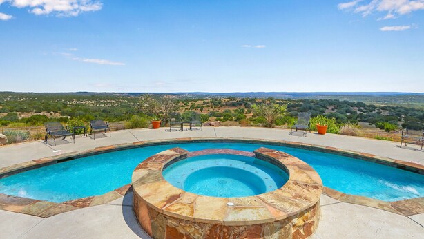 Ein Swimmingpool mit Whirlpool, umgeben von Liegestühlen und Topfpflanzen, mit Blick auf eine reizvolle Landschaft.
