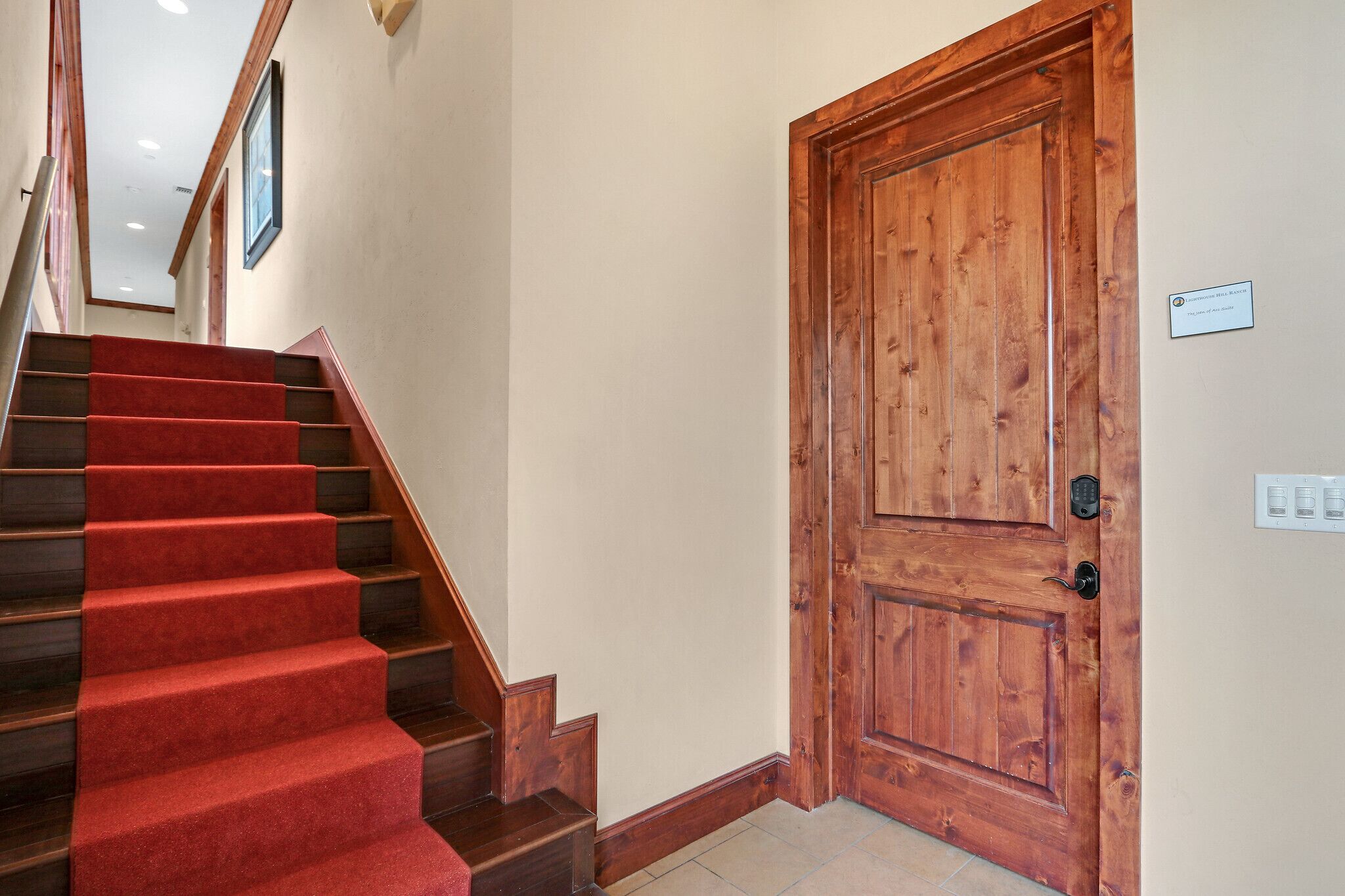Un escalier recouvert d’une moquette rouge mène à une porte en bois.