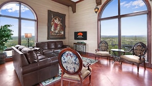 A spacious living room with leather sofas, a large painting, and a view of the countryside through large windows.