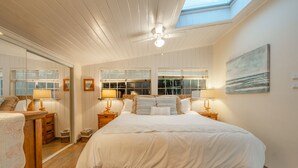 Une chambre avec un grand lit, un plancher en bois, une lucarne et un tableau au mur.