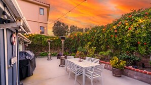 Une terrasse avec une table et des chaises, entourée d’un mur de briques et de plantes en fleurs.