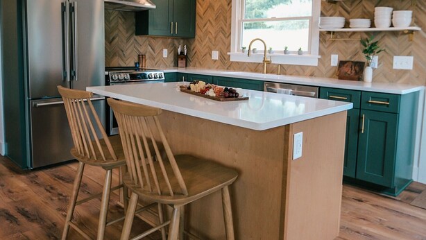 Una cocina moderna con una isla central, sillas de madera y armarios verdes.