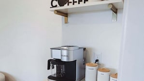 Una kitchenette con una cafetera Keurig, un estante para café y recipientes etiquetados para café, té y azúcar.