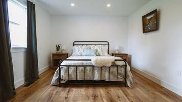 Une chambre avec un plancher en bois, un cadre de lit en métal, deux tables de chevet avec des lampes et un tableau au mur.