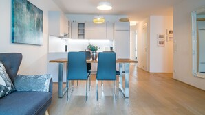 A modern kitchen with white cabinets, a wooden dining table, and blue chairs. - Vienna Residence, Pramergasse - Inner City #6325 (Vienna)