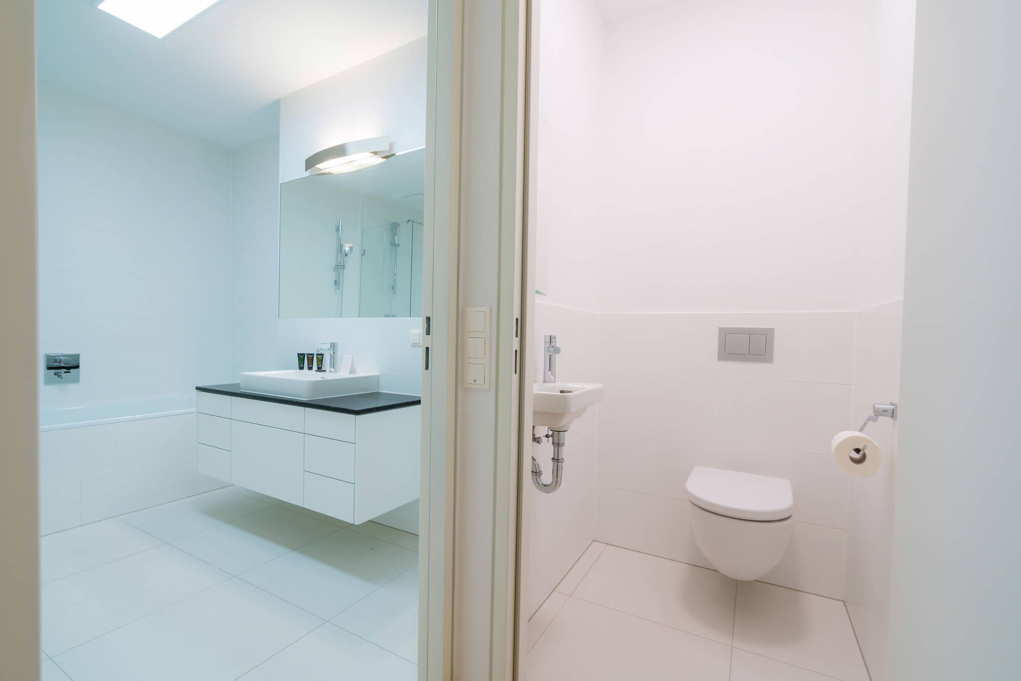 Ein modernes Badezimmer mit Waschbecken, Spiegel und Toilette in Weiß.