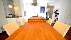 A modern kitchen with white cabinets, a wooden dining table with six chairs, and a central island. - Vienna Residence, Steckhovengasse - Hietzing #4888 (Vienna)