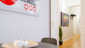 A modern dining area with a round table, a bowl with apples, and a wall with a red and black abstract painting.