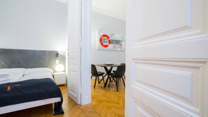 A hotel room with a bed, bedside table, lamp, and a dining area with chairs and a table.