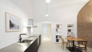 A modern kitchen with a stainless steel sink, a dining area with a wooden table and chairs, and a brick wall. - Vienna Residence, Wasagasse - Alsergrund #6294 (Vienna)