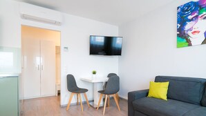 Una sala de estar moderna con un sofá gris, un televisor de pantalla plana montado en la pared y una pequeña mesa con dos sillas.
