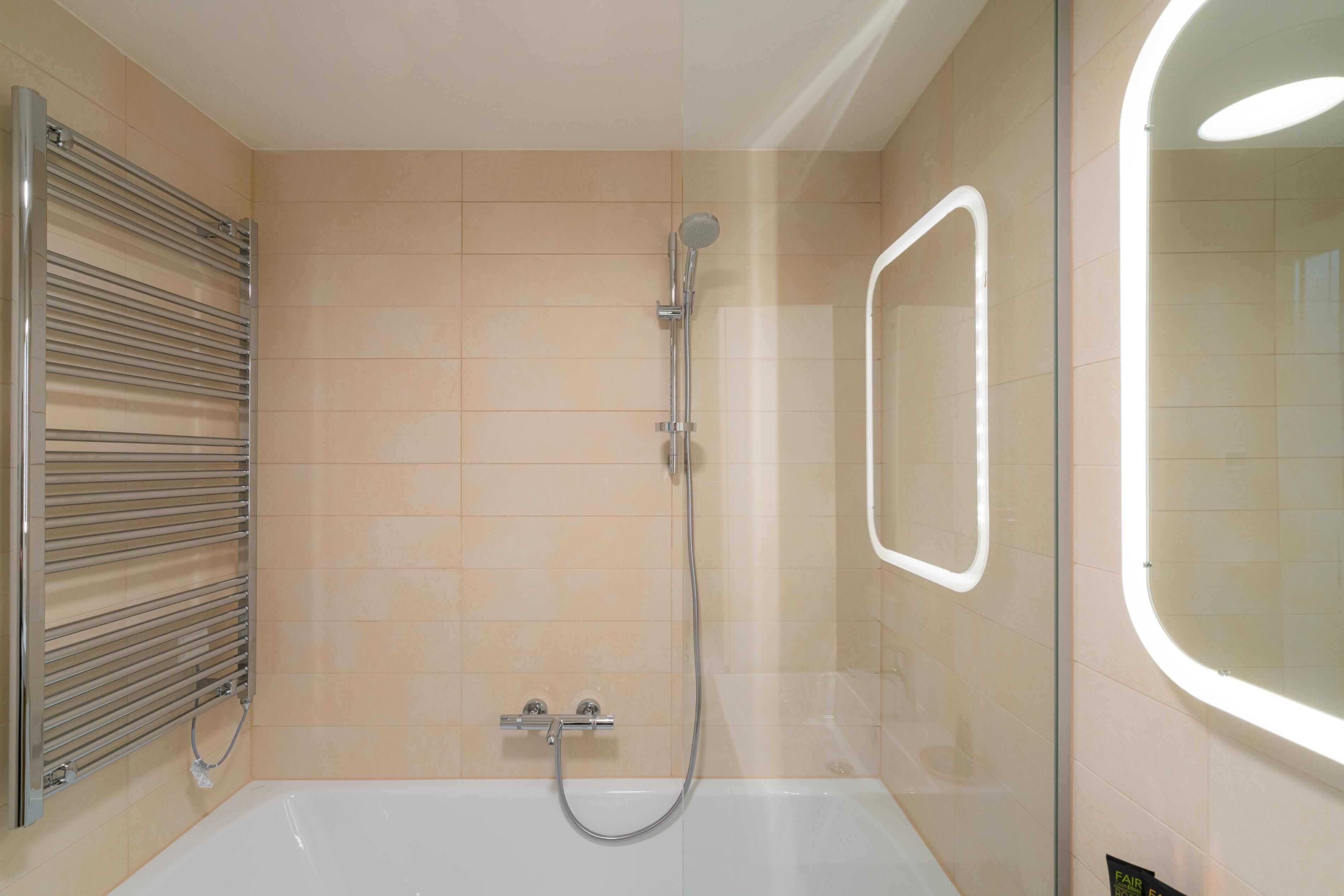 A modern bathroom with a bathtub, a shower with a handheld showerhead, and a wall-mounted towel rack.