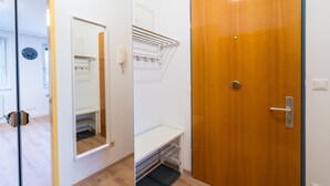 Ein Zimmer mit Holztür, weißer Wand, Spiegel und einer kleinen Sitzbank.