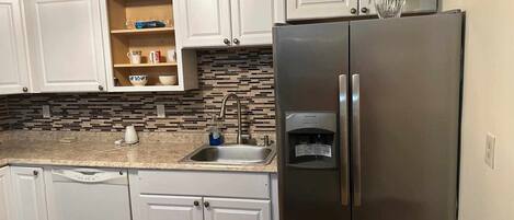 Una cocina con armarios blancos, un refrigerador de acero inoxidable, un lavamanos y un dispensador de agua.