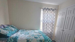 A bedroom with a bed, a window with patterned curtains, and a door. - Room G Divine Villa and Resorts (Newark)