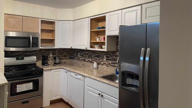 A kitchen with white cabinets, a stainless steel refrigerator, a microwave, and a stove. - Room G Divine Villa and Resorts (Newark)