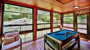 Una mesa de billar en una habitación con ventanas amplias que dan a un área boscosa.
