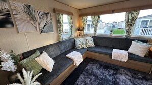 A cozy living room with a dark grey sectional sofa, decorative pillows, a black furry rug, and artwork on the walls. - A Beautiful, Dog Friendly Holiday Home (Mablethorpe)