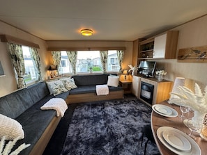 Ein gemütliches Wohnzimmer mit einer Eckcouch, einem Kamin und einem Essbereich mit Tellern und Gläsern.