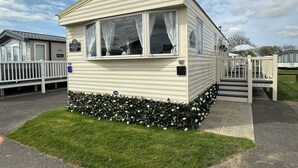 A mobile home with a front porch, a small garden area, and a clear sky. - A Beautiful, Dog Friendly Holiday Home (Mablethorpe)