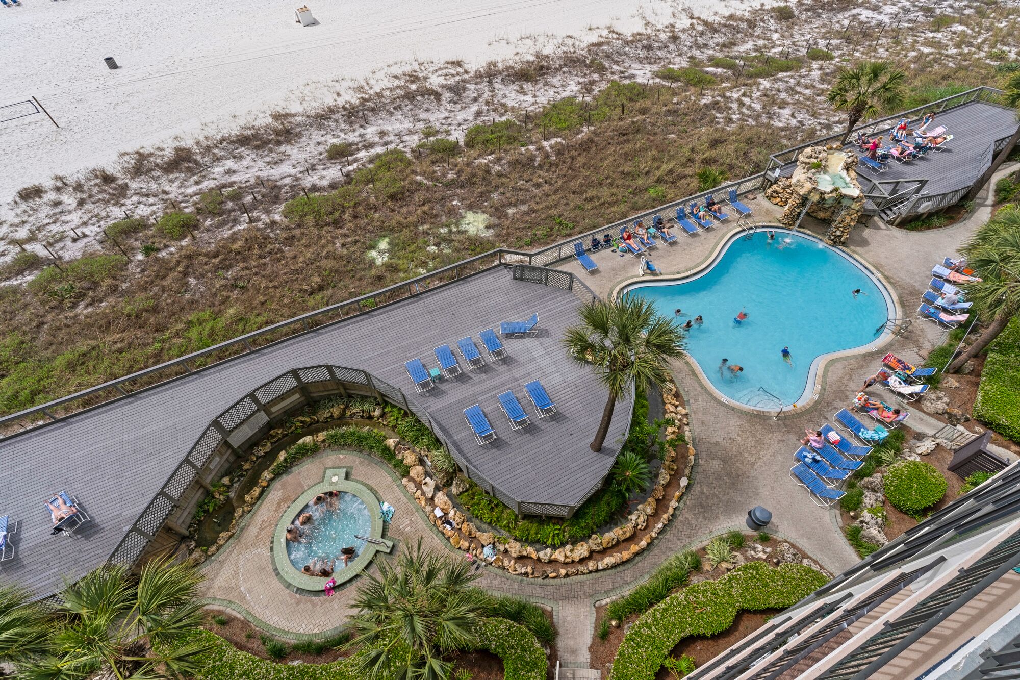 Vue aérienne d’un complexe hôtelier doté d’une grande piscine, de chaises longues et d’un petit jacuzzi.