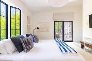 A bedroom with a large bed, a desk, and a view of greenery through the windows. - Secluded 3-Bedroom Luxury Retreat near Beach – Perfect Getaway! (Douglas)