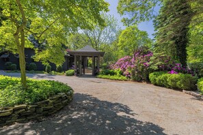 A gazebo in a garden with a stone wall and flowering bushes.