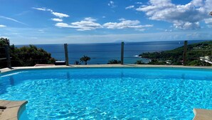 A clear blue pool with a view of the ocean and a wooden deck. - Espace Harmonie vue mer (Deshaies)