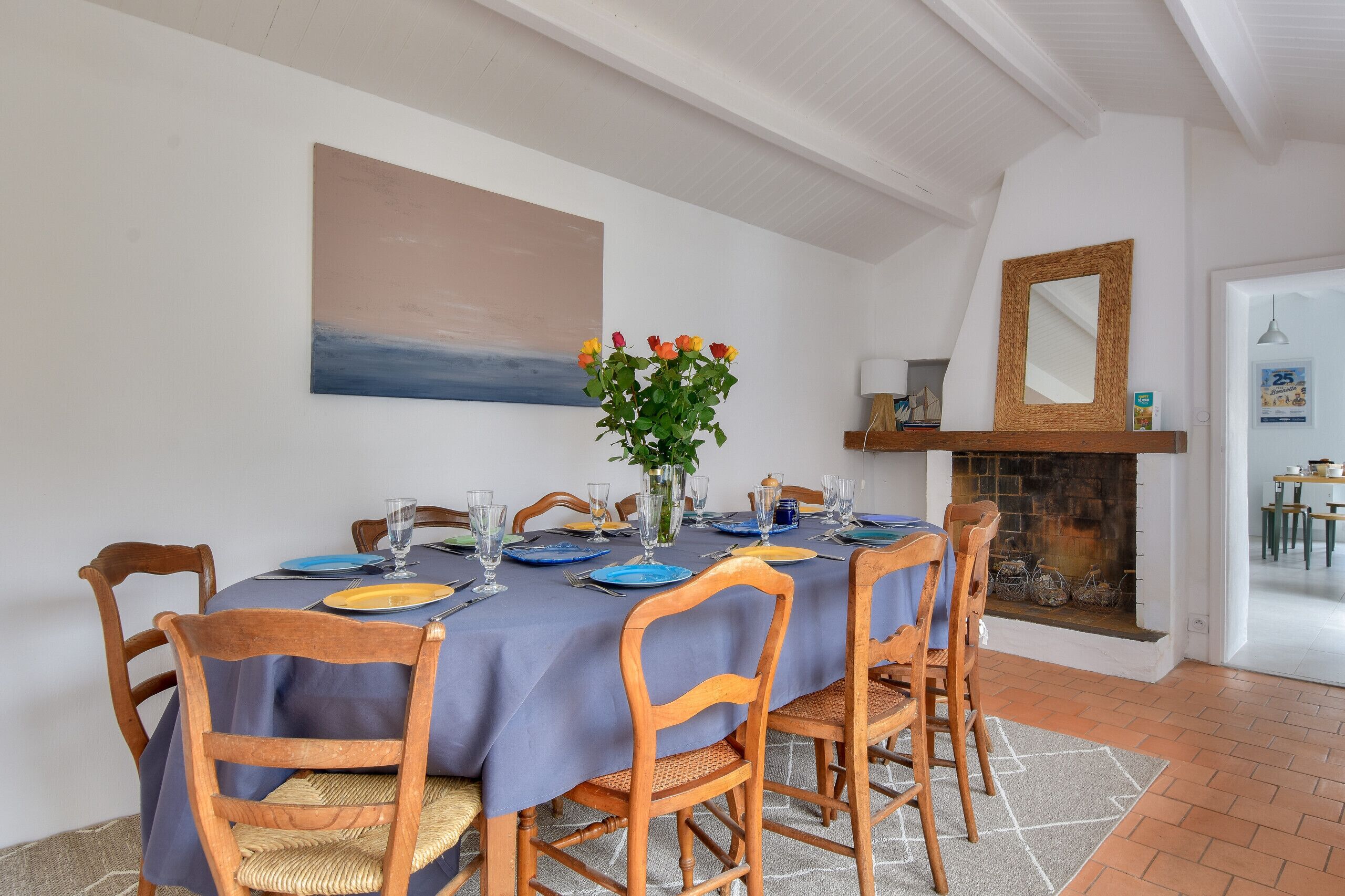 Una sala da pranzo con tavolo apparecchiato per quattro persone, sedie di legno, tovaglia blu e un vaso con fiori.