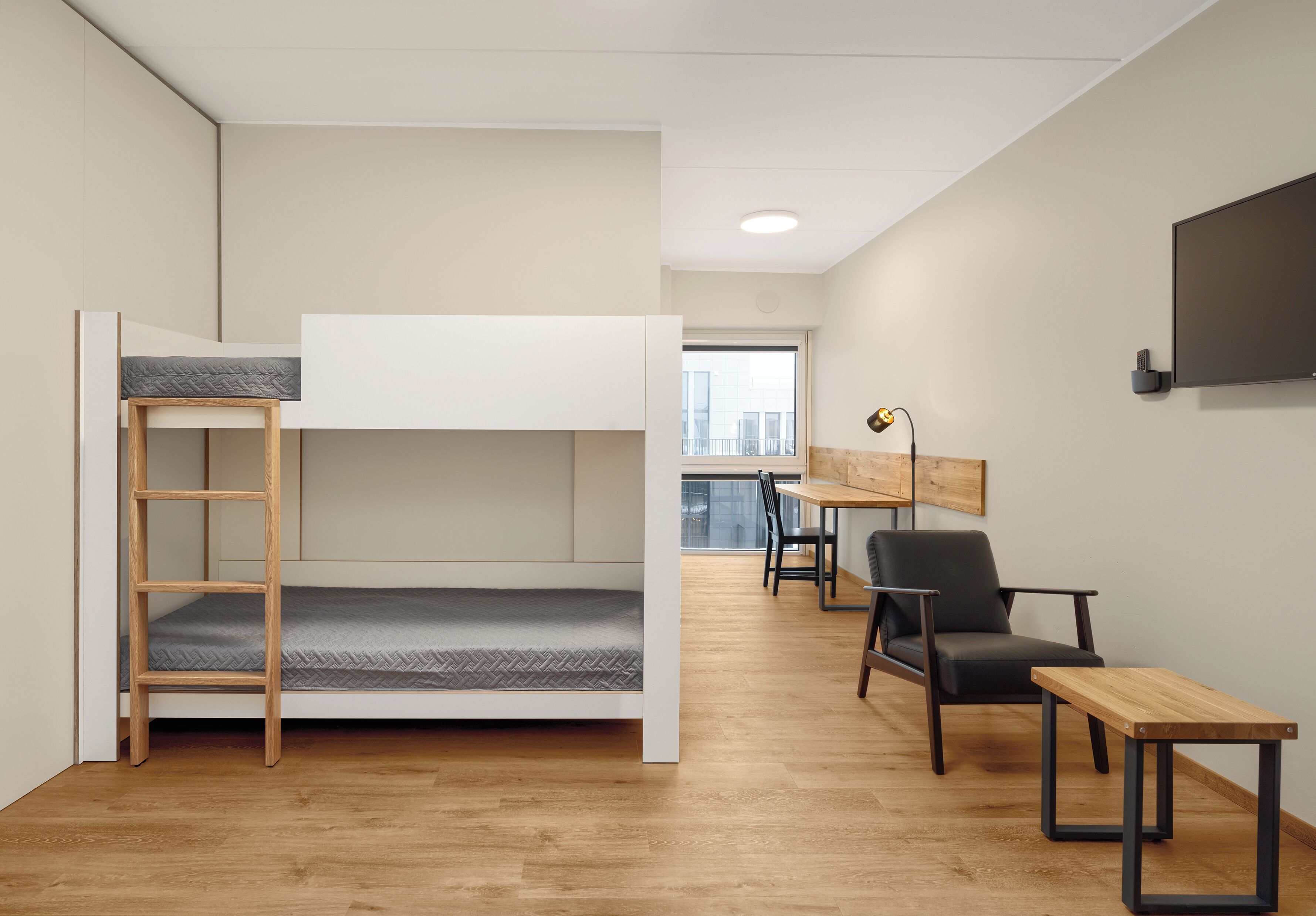 A modern, minimalist room with a bunk bed, a desk, a chair, and a small table.