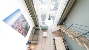 A modern loft apartment with a large window, a cityscape view, a staircase, and a minimalist interior design.
