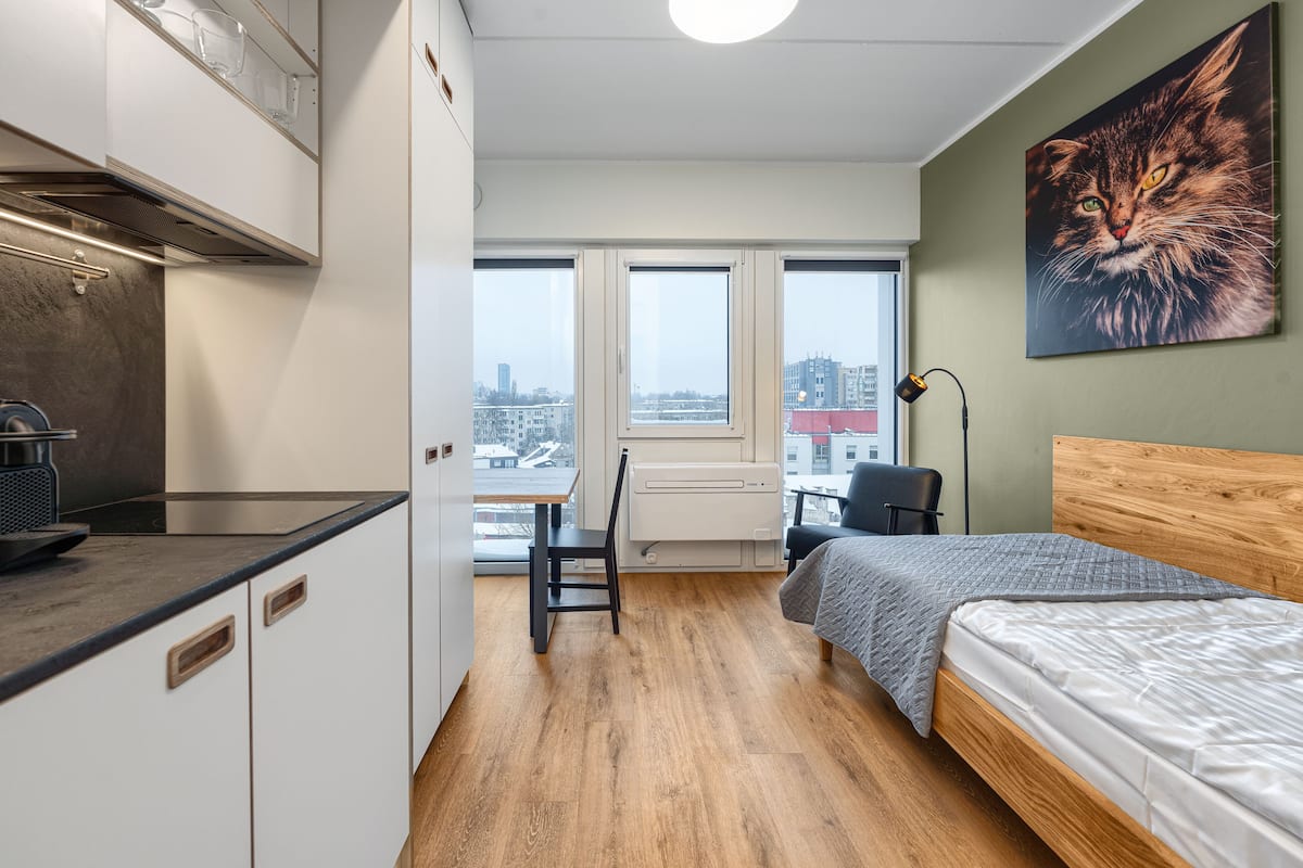 Ein modernes Schlafzimmer mit einem Holzkopfteil, einem Bett, einem Schreibtisch und Blick auf die Stadt durch große Fenster.
