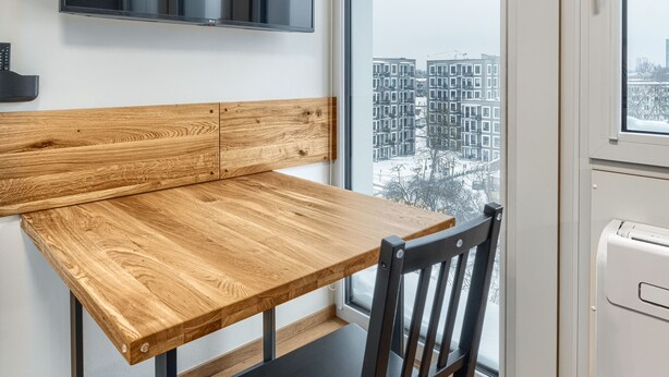 A modern kitchen with a wooden table and black chairs, a built-in microwave, and a large window offering a view of a cityscape.