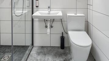 Un bagno moderno con box doccia in vetro, lavandino bianco, water e specchio con ripiano in legno sopra.