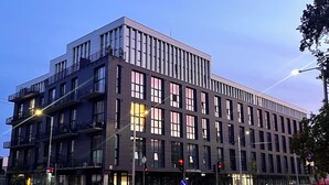 A modern multi-story building with large windows and balconies, located at a street corner.