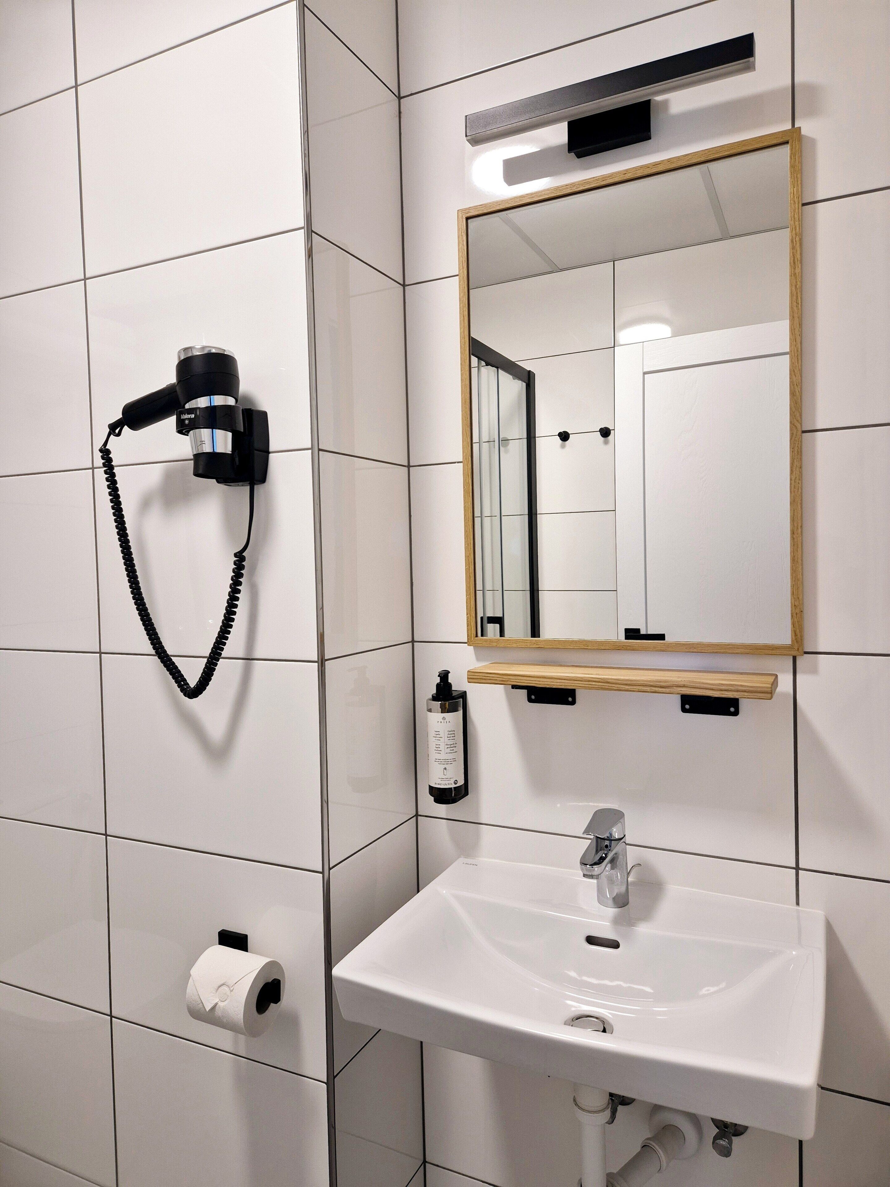 A bathroom with a white sink, a mirror, a hairdryer mounted on the wall, and a toilet paper roll.
