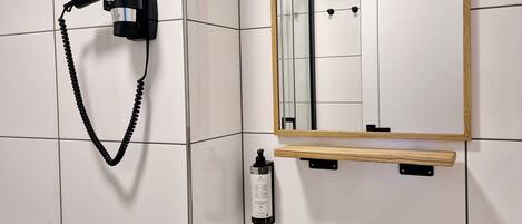 A bathroom with a white sink, a mirror, a hairdryer mounted on the wall, and a toilet paper roll.