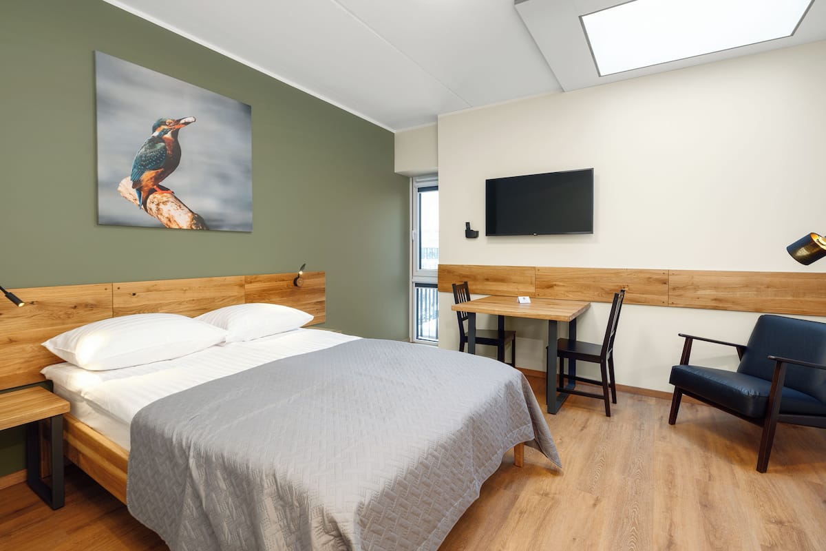 Ein Hotelzimmer mit Bett, Schreibtisch, Stuhl, Fernseher und einem Vogelgemälde an der Wand.