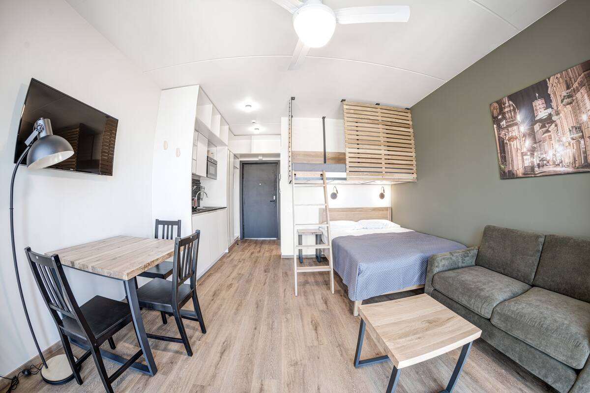 Ein kleines Zimmer mit Etagenbett, Schreibtisch mit Stühlen, einer Couch und einem Deckenventilator.