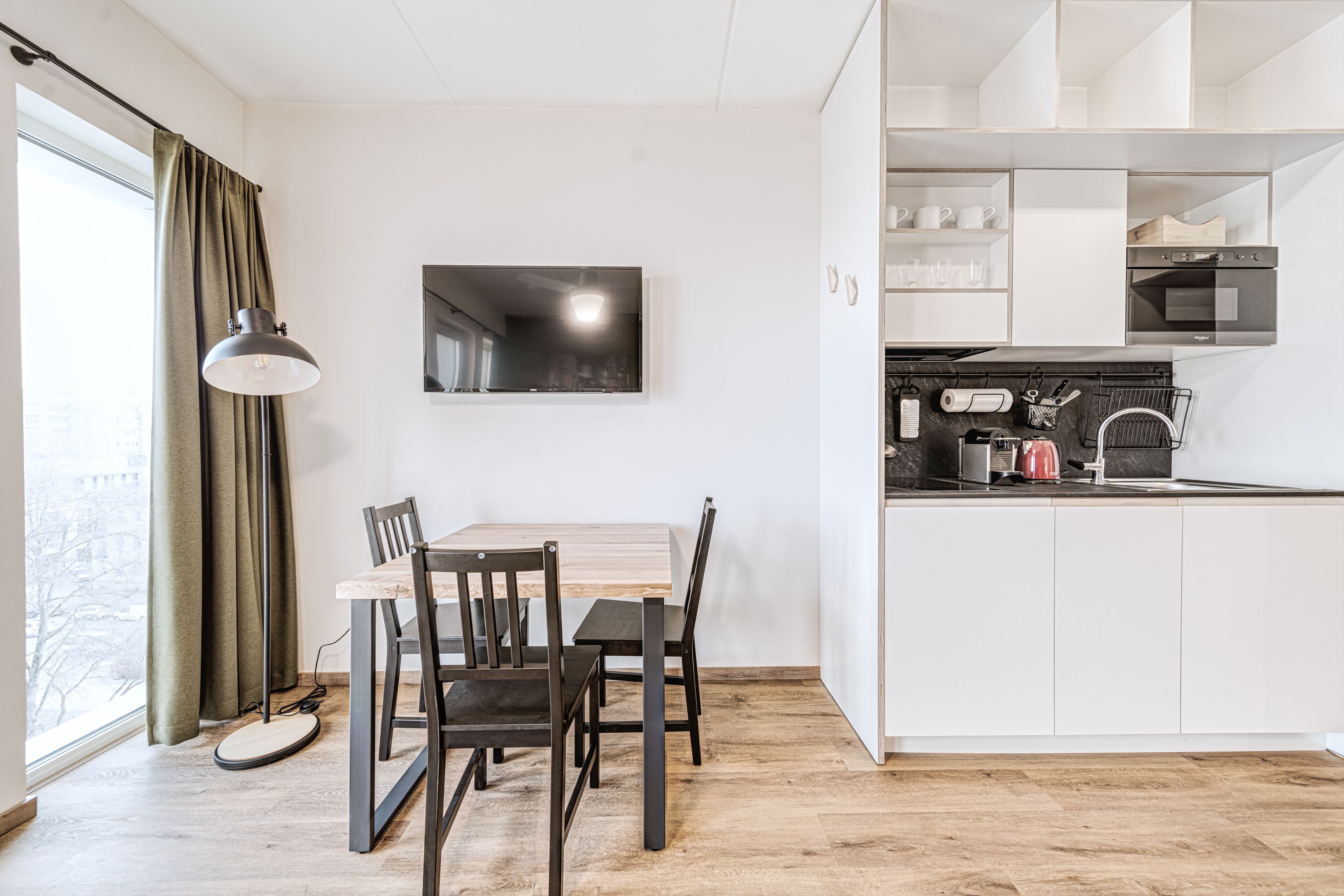A modern kitchen with white cabinets, a black stove, and a dining area with a wooden table and chairs.