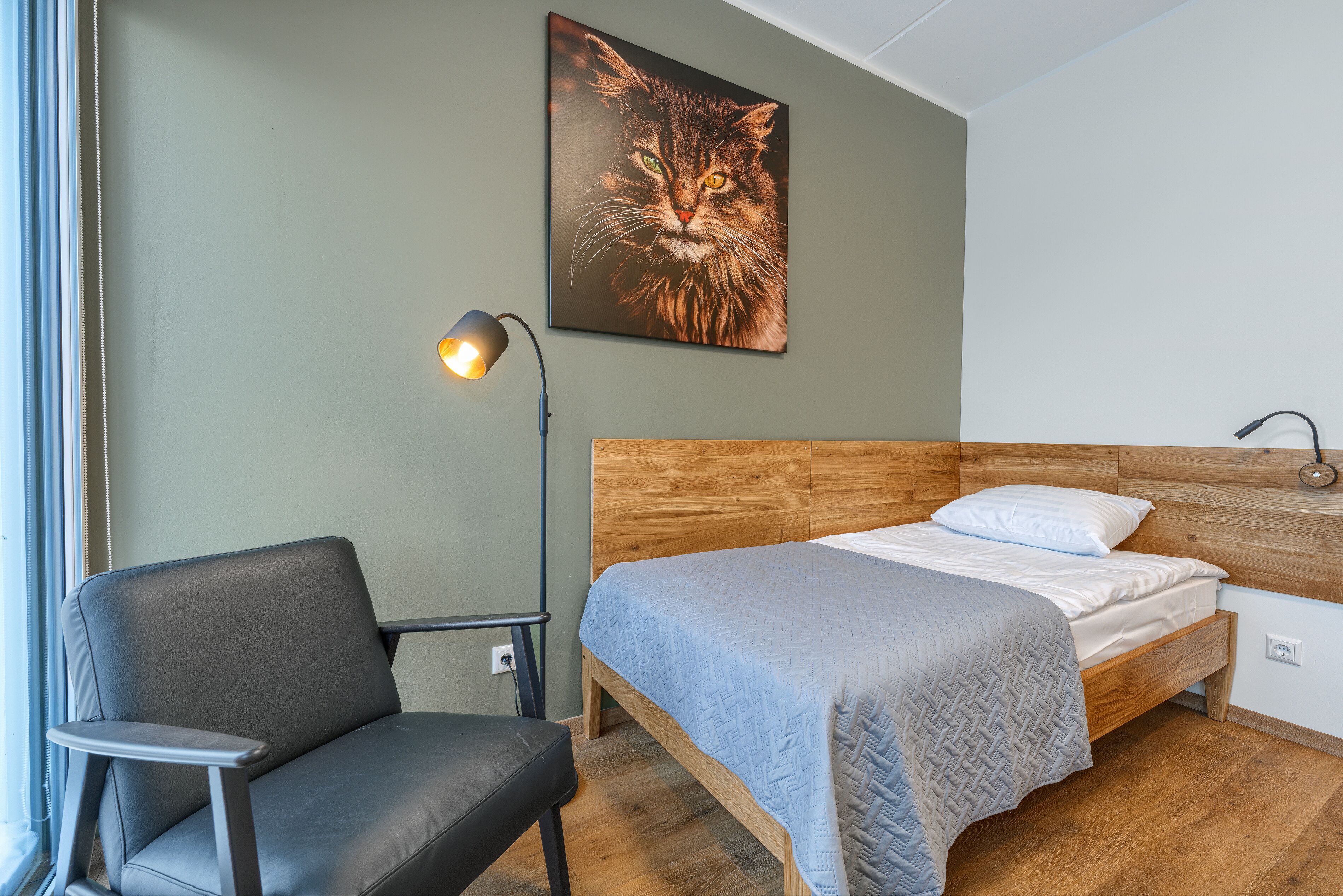 A bedroom with a wooden bed, a grey chair, and a wall-mounted lamp.