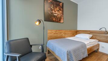Un dormitorio con una cama de madera, una silla gris y una lámpara fijada a la pared.