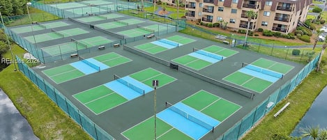 Un complexe de courts de tennis comprenant plusieurs terrains, entouré d’une clôture et situé à côté d’un immeuble d’habitation.