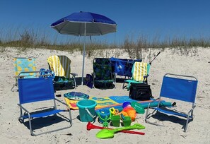 Strandaufstellung mit zwei blauen Liegen, einem blauen Sonnenschirm sowie verschiedenen Strandspielzeugen und Ausrüstung.
