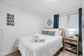 Ein ordentlich eingerichtetes Schlafzimmer mit einem Bett, einem Nachttisch mit Lampe und einem kleinen Regal mit Büchern.