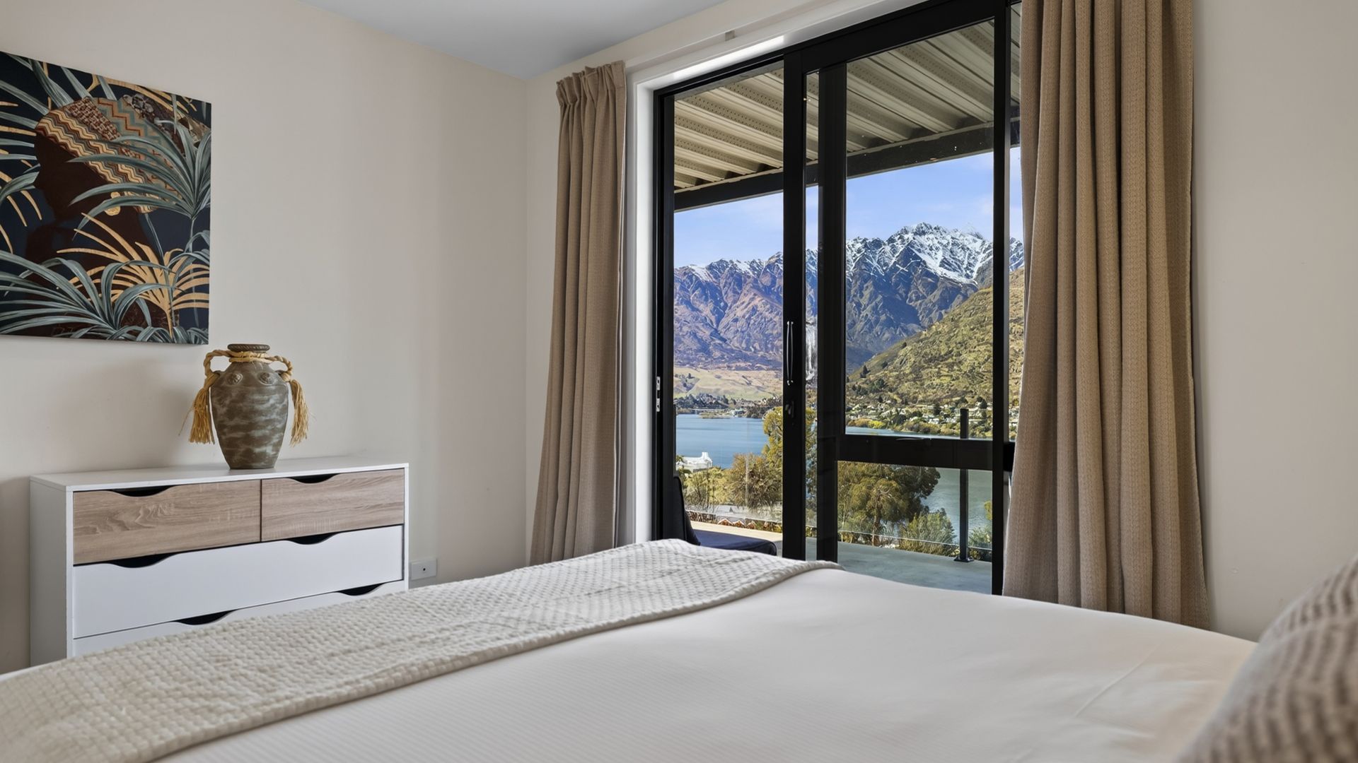 Een slaapkamer met een groot raam, een bed, een dressoir en een vaas.