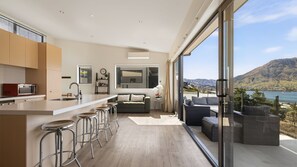Una cocina moderna con una isla central, taburetes de bar, un sofá y vistas a un paisaje montañoso.